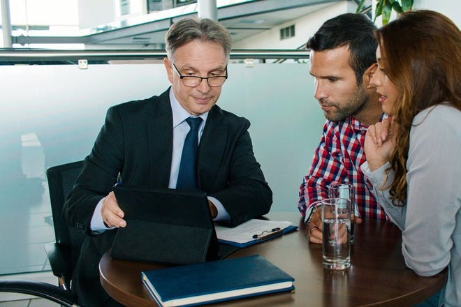 A couple meets with a financial advisor, looking anxiously at a tablet screen.