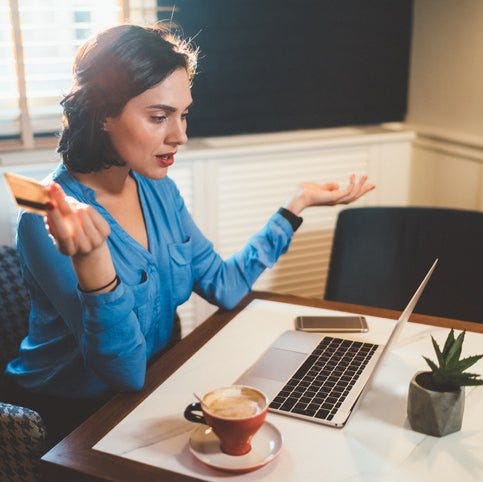 A woman looking frustrated with a credit card in her hand while looking at a laptop.