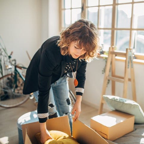A woman packing moving boxes in a sunny apartment.