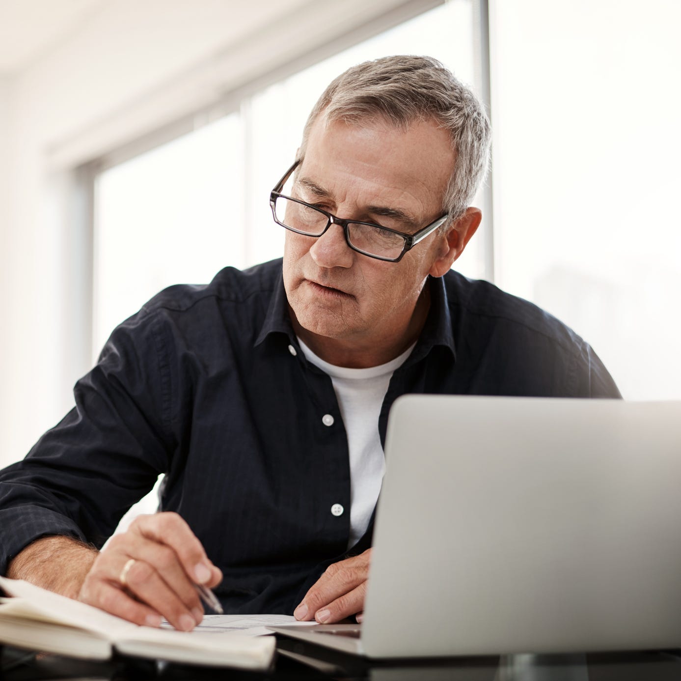 Person writing on a notepad in front of a laptop.