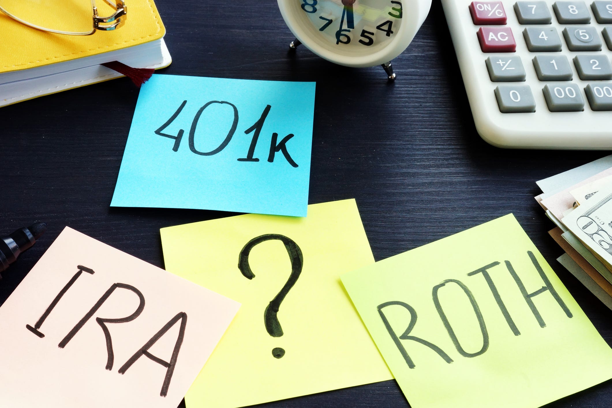Post-it notes on a desk labeled 401k, IRA, and Roth, with a big question mark in the middle.