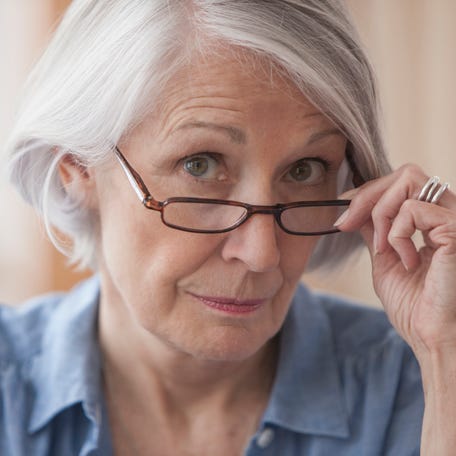 A person pulling eye glasses down with a skeptical expression.