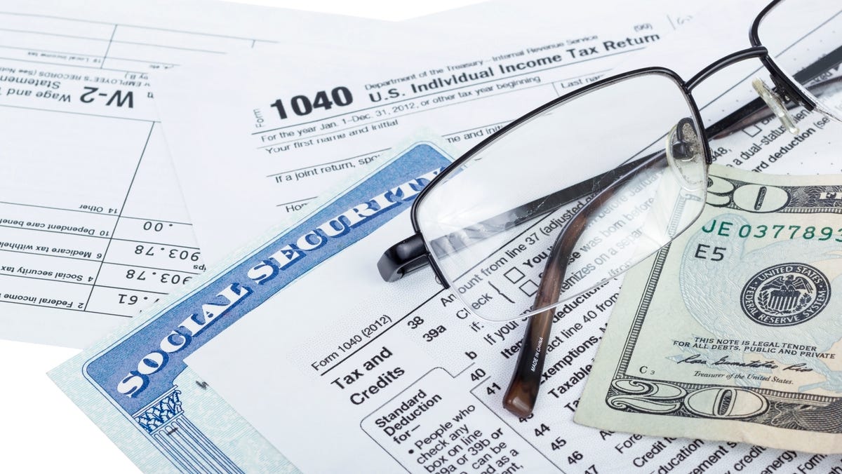 A pair of glasses, a twenty-dollar bill, and a Social Security card, set atop federal income tax forms.
