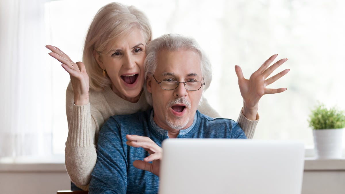 A couple is looking at an open laptop, mouths open in happy surprise.