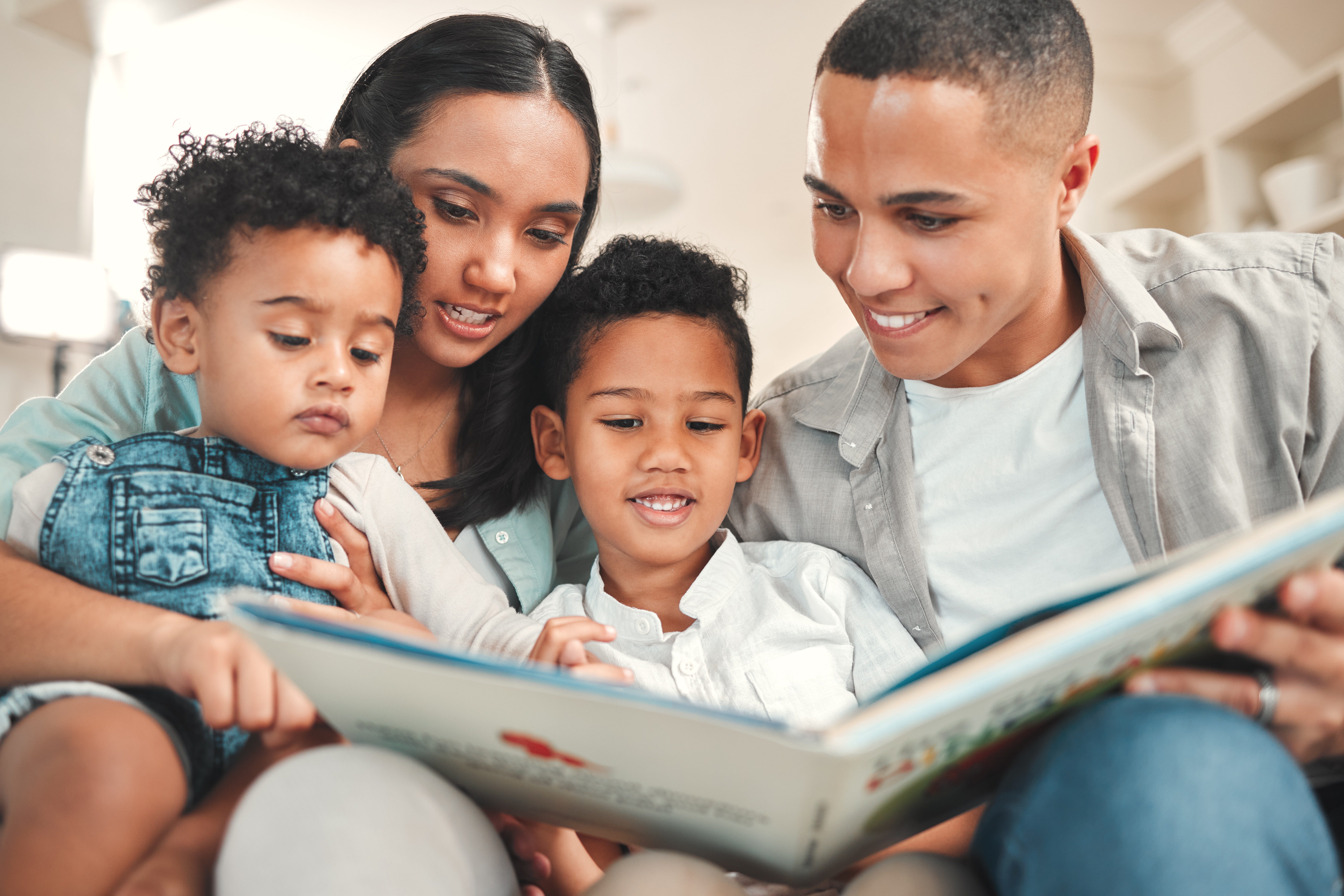 Two adults and two children sitting down and looking at a book.