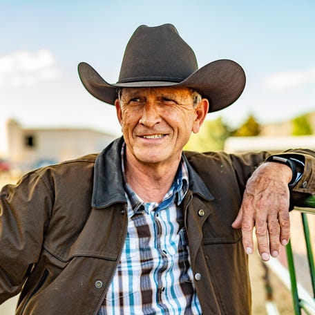 A person in a cowboy hat is resting his arm on a fence, looking into the distance.