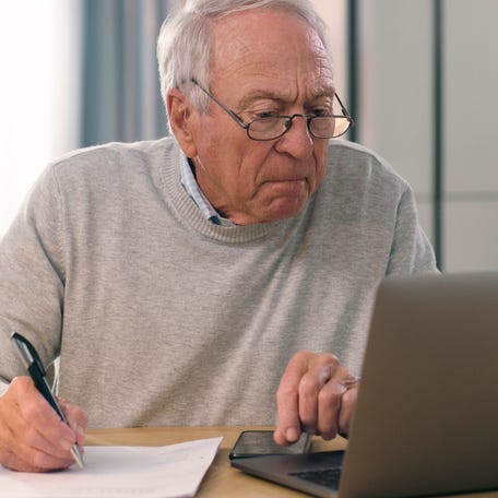 Person staring at laptop and writing note on paper.