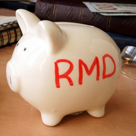 A cluttered desk with a piggy bank sitting on top. On the side of the piggy bank are the letters "RMD."