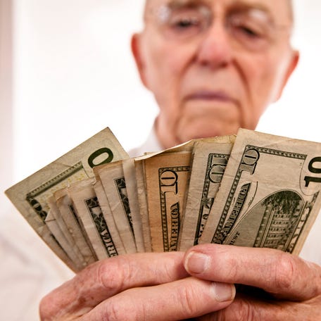 A seated person counting a fanned assortment of cash bills in their hands.
