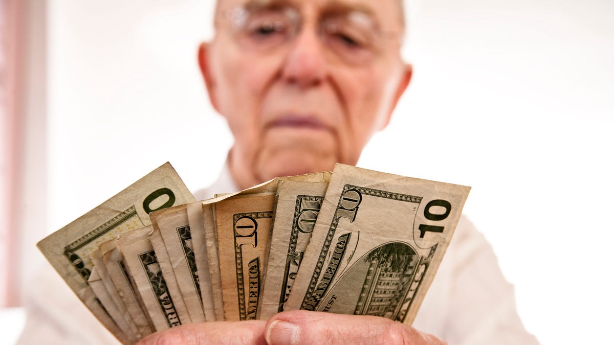 A seated person counting a fanned assortment of cash bills in their hands.