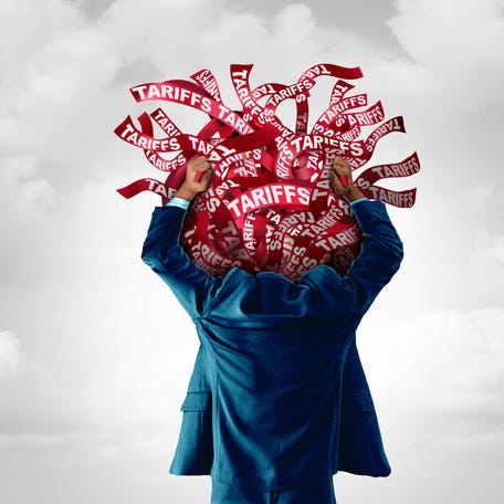 A person wearing a suit holds a tangle of red ribbons that say Tariffs above their head.