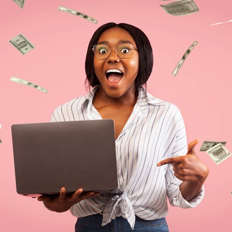 Happy investor pointing to a laptop while dollar bills fly in the air.