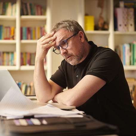 Worried-looking person sitting at a desk, looking at a laptop.