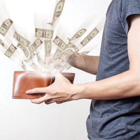 Person holding wallet with cash flying out of it.