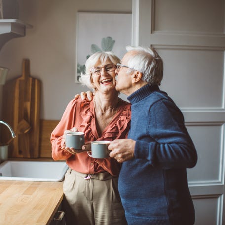 Someone kissing another person on the cheek while both hold coffee mugs.