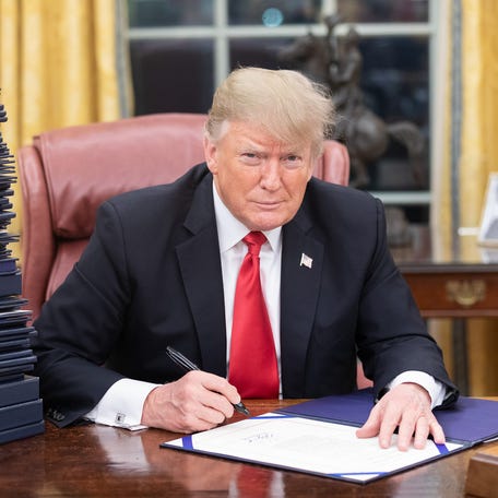 Donald Trump signing a bill while seated at a desk in the Oval Office.