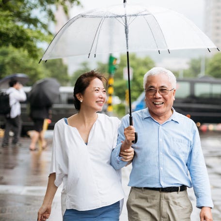 A couple is walking in a city, holding an umbrella and smiling.