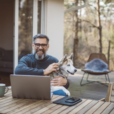 A person at a laptop holding a dog.