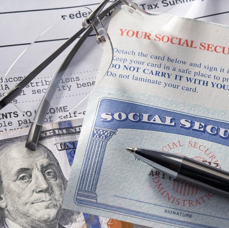 A pen laying on top of a Social Security card on top of eyeglasses, a $100 bill, and financial statements.