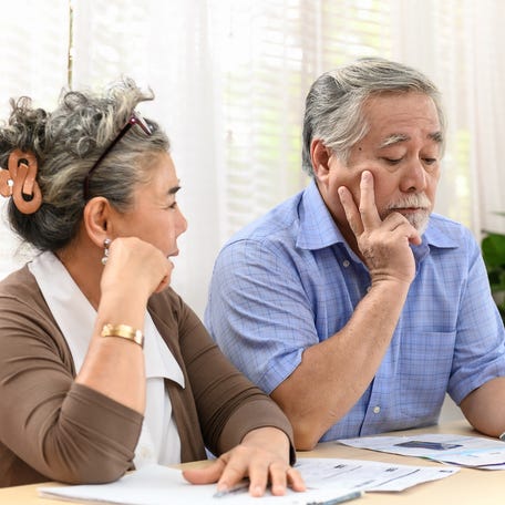 A visibly worried couple examining bills and financial statements while seated at a table in their home.