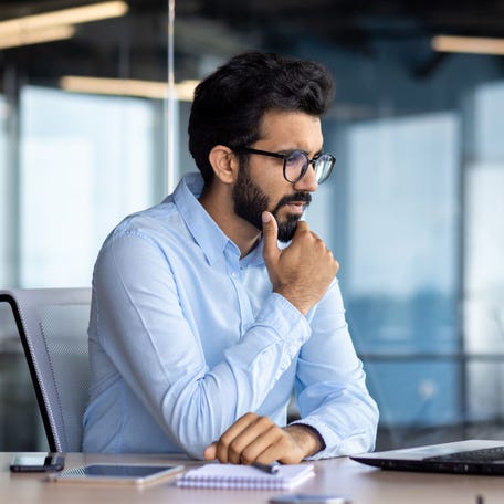 Investor thinking while sitting in front of a laptop.