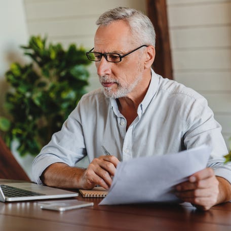 A person at a laptop holding papers.