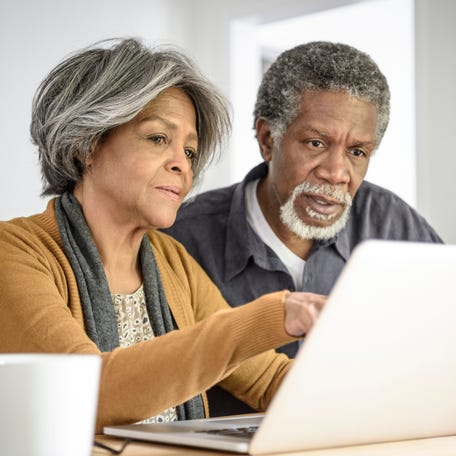A couple critically reading content from a shared laptop while seated at a table in their home.