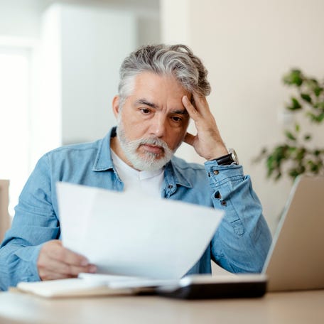 A person at a laptop with a serious expression holding a document.