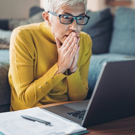 A shocked person staring at a laptop with their hands over their mouth.