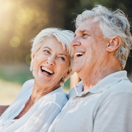 Two people laughing and sitting on bench holding hands.