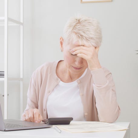A person at a table with a laptop holding their head.