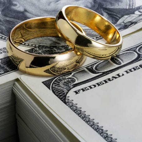 Stacks of cash with two gold wedding rings balanced on top.