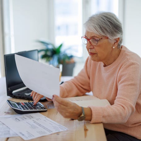 An older adult sitting at a desk while doing computations with a calculator.
