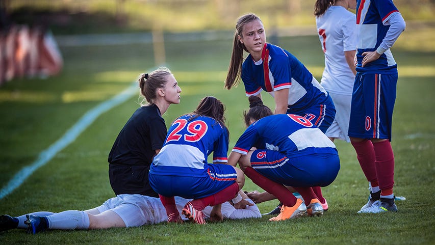 A trainer and players tend to an injured female soccer player