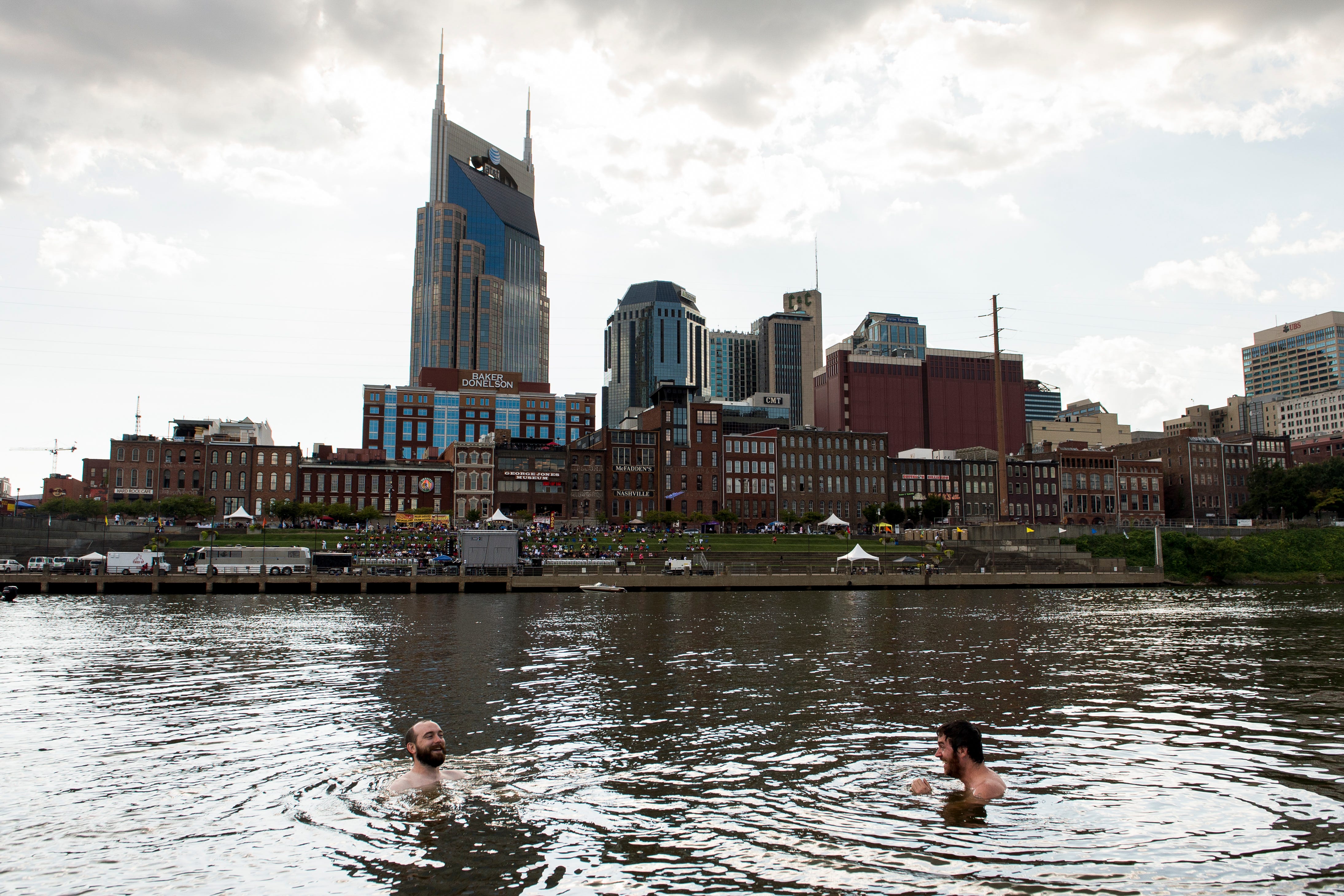Blair McMillan, left, of Nashville, and Vaughn Walters, right, of Nashville, go for a swim in the Cumberland River across from the downtown skyline, in Nashville, Tenn.