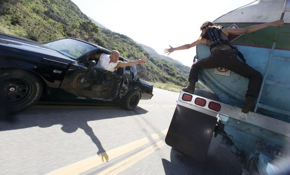 Vin Diesel and Michelle Rodriguez reaching out to each other in an action-packed scene from "Fast & Furious."
