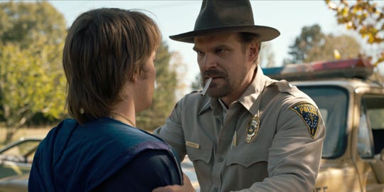 Charlie Heaton, left, and David Harbour, with a cigarette in his mouth, co-star in a scene from Netflix's "Stranger Things."