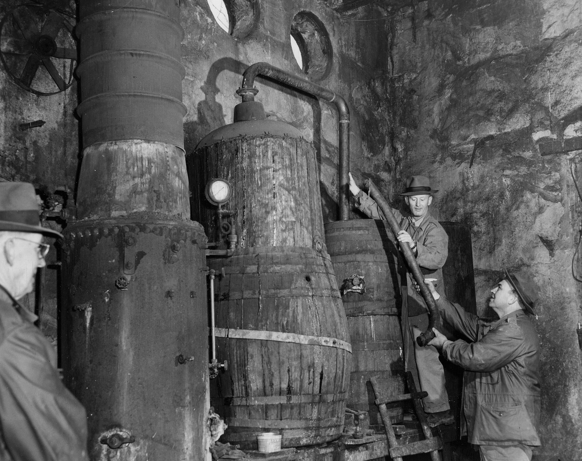 Dismantling a 300-gallon moonshine still found in a raid near Crestwood are Elmer C. Davis and Mark Holmes, agents of the Federal Alcohol Tax Unit. At left is a steam boiler, and in center is the actual still. March 4, 1951