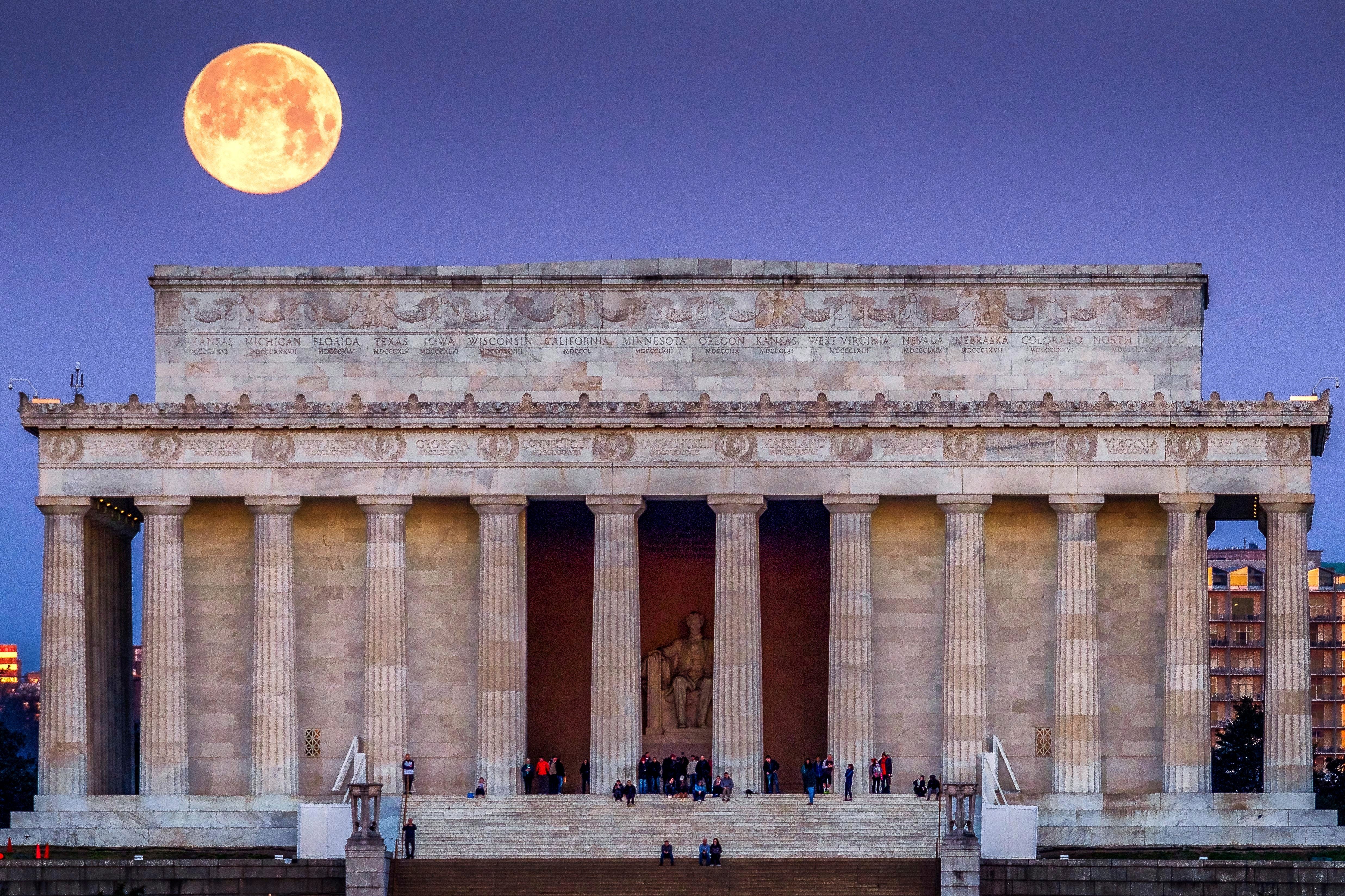 The full moon sets behind the Lincoln Memorial as people line the steps to watch the sun come up across the other end of the National Mall in Washington.