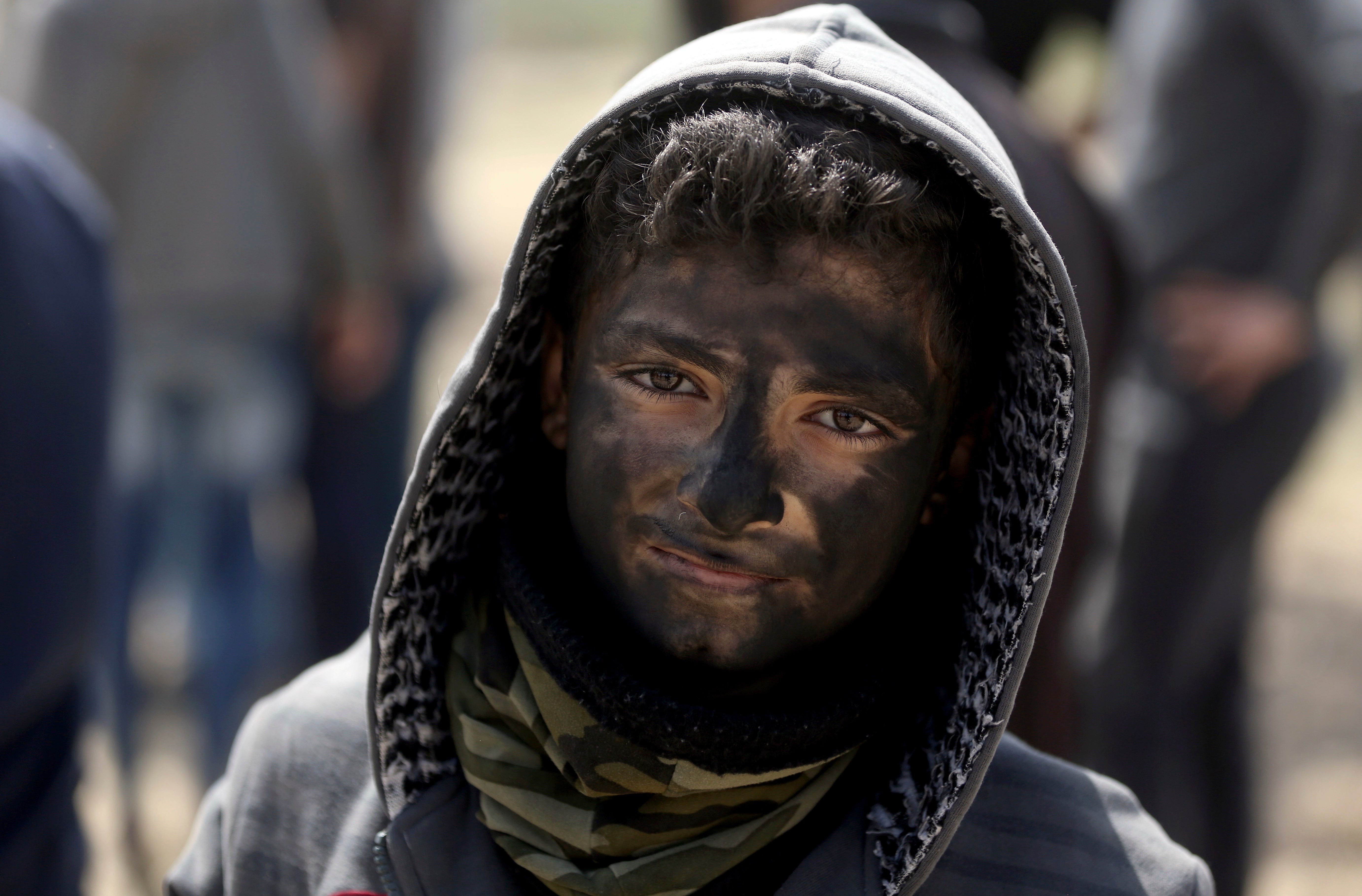 A Palestinian boy poses for a photograph as he paints his face in black during a protest at the Gaza Strip's border with Israel.