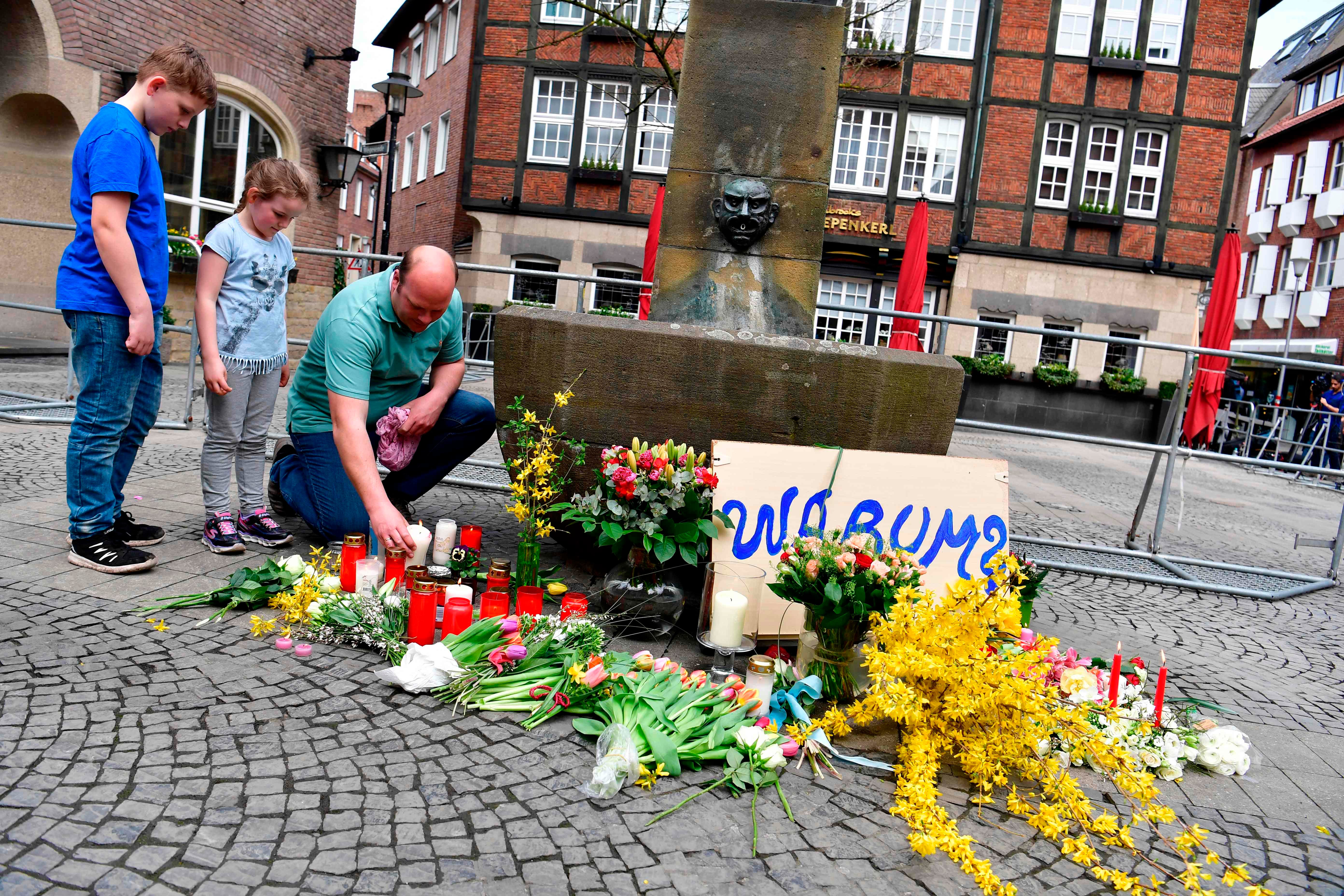 A man and children lay flowers on April 8, 2018 at a memorial at the square where a man drove a van into an open-air restaurant, killing two people a day earlier in Muenster, Germany.