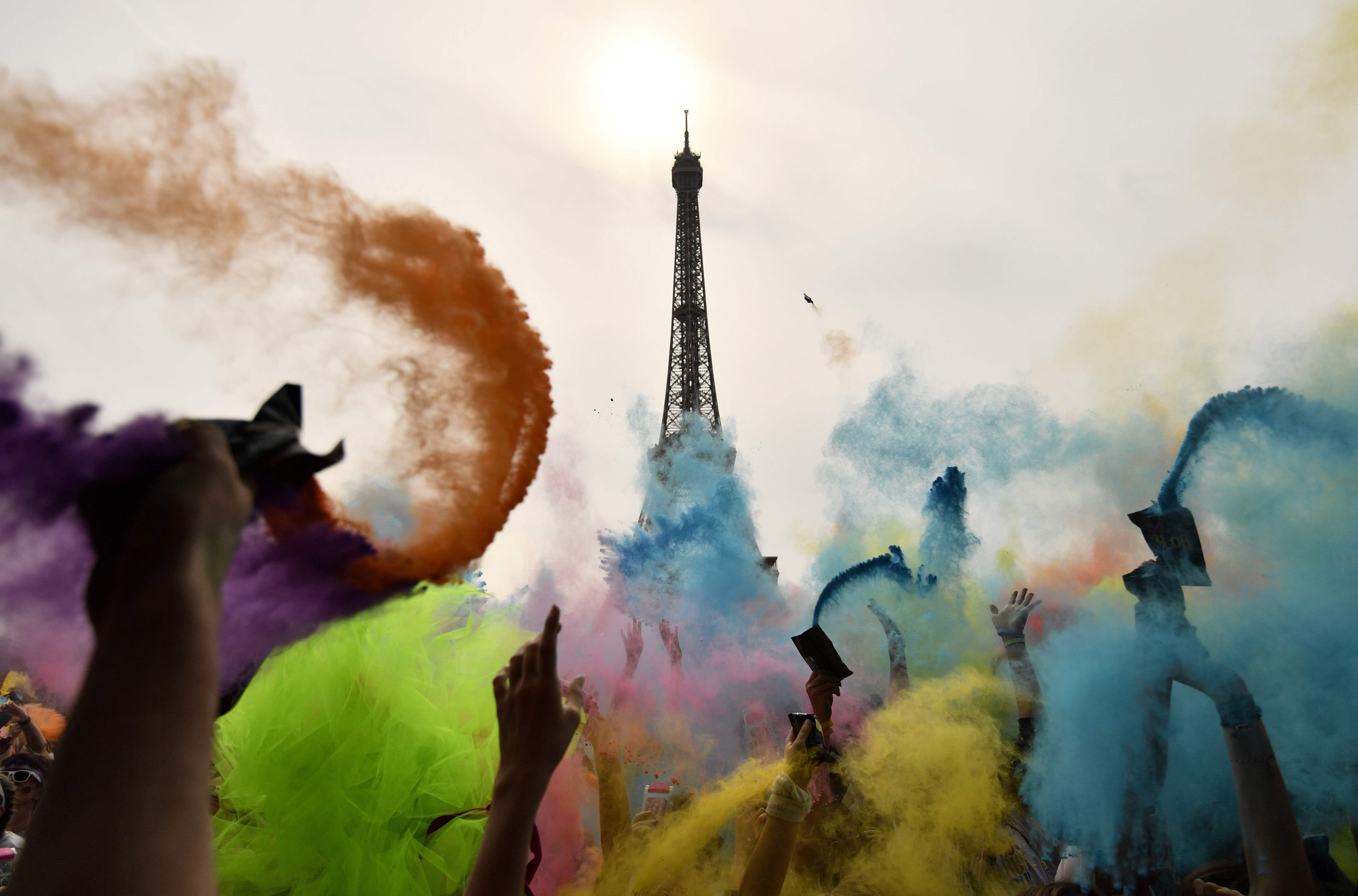 People throw colored powder as they celebrate at the end of the Color Run 2018 race in front of the Eiffel Tower in Paris, on April 15, 2018.The Color Run is a three mile paint race without winners nor prizes, while runners are showered with colored 