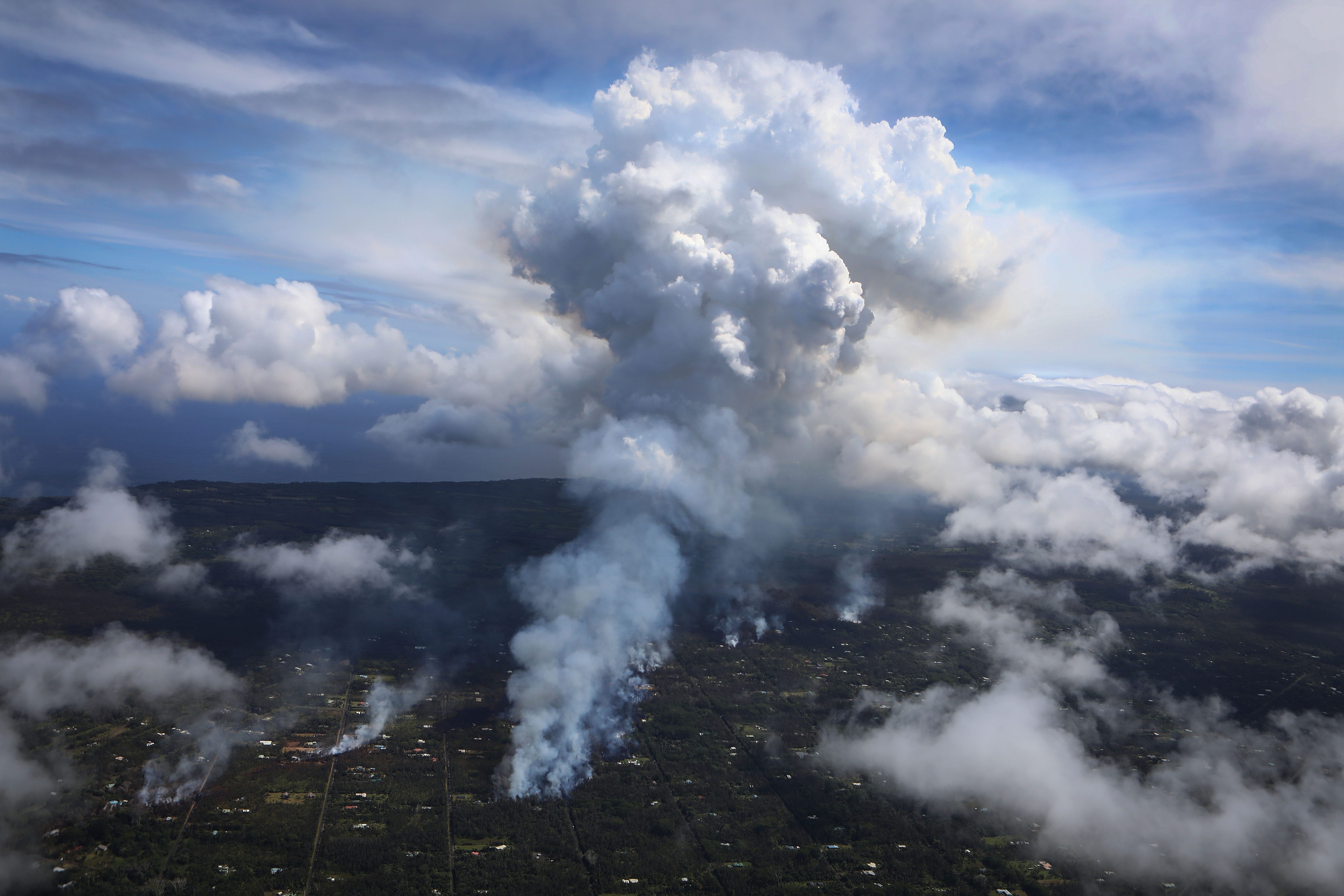 A plume of volcanic gas mixed with smoke from fires caused by lava rises (C) amidst clouds in the Leilani Estates neighborhood in the aftermath of eruptions from the Kilauea volcano on Hawaii's Big Island on May 6, 2018 in Pahoa, Hawaii. A magnitude 