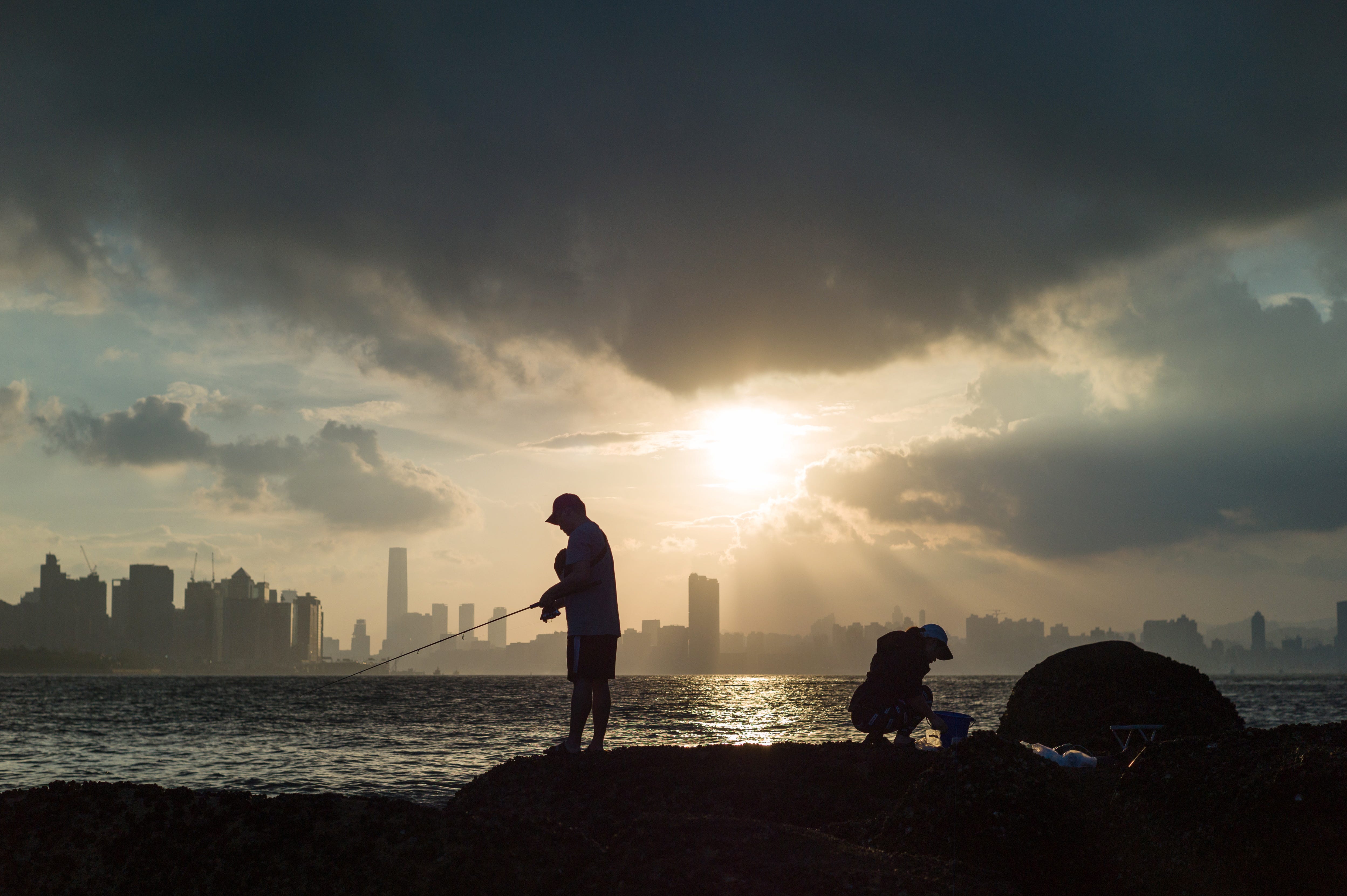 A man fishes as the sun sets over Victoria Harbor from the shoreline Lei Yu Mun in Hong Kong, China.