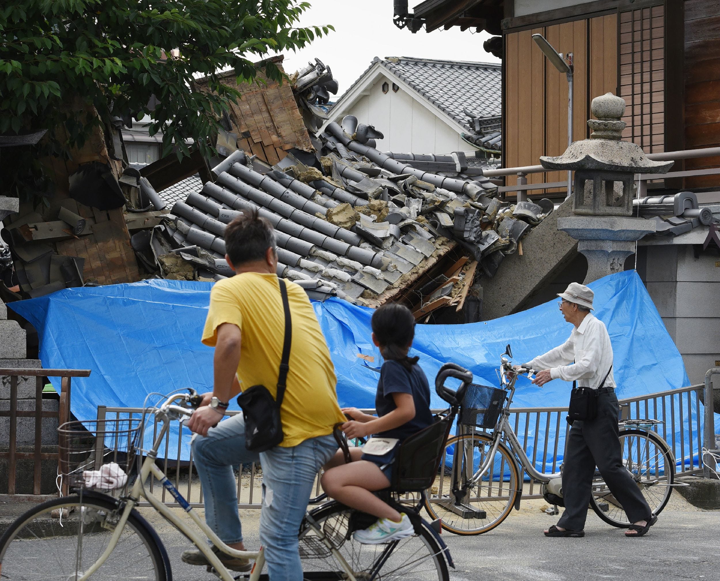 People pause to look at a collapsed house following an earthquake in Ibaraki, north of Osaka prefecture on June 18, 2018.  At least two people, including a child, were killed on June 18, after a strong quake rocked the city of Osaka during the morning