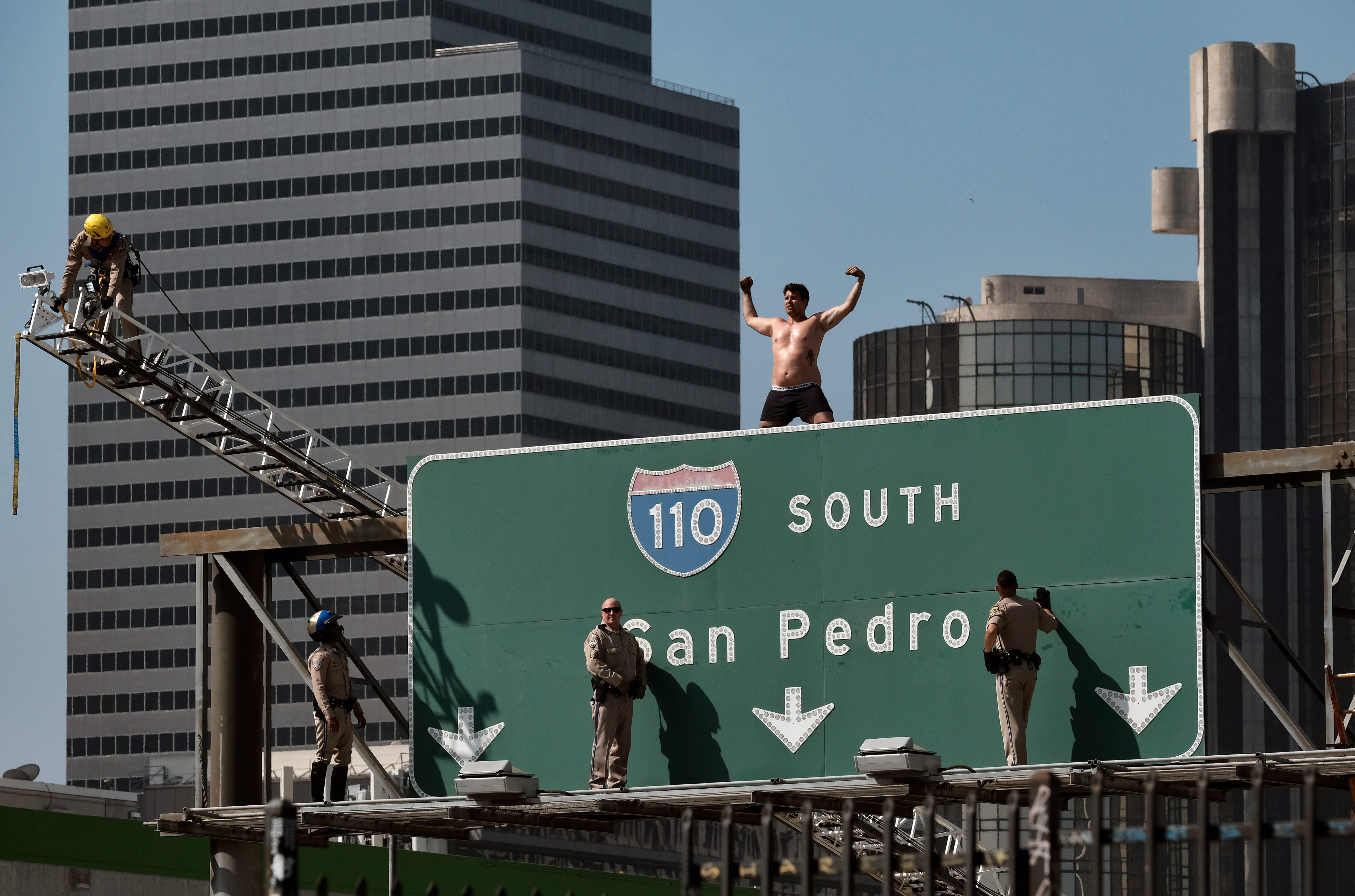 California Highway Patrol officers try to coax a man off a freeway sign in downtown Los Angeles. The man suspended banners, one about fighting pollution, after climbing onto the sign over State Route 110 during  morning rush hour.