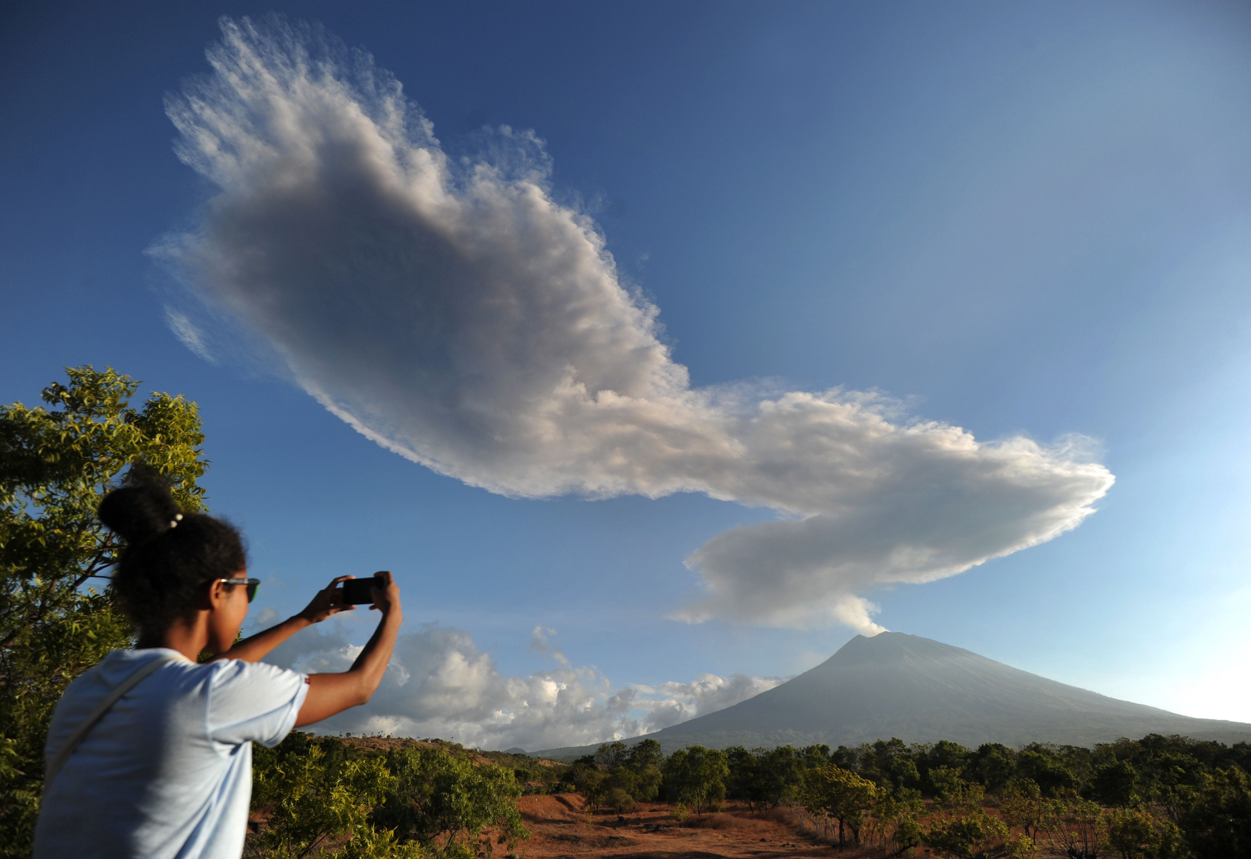 A woman photographs the Mount Agung volcano sending up a plume of smoke on Indonesia's resort island of Bali. Mount Agung roared to life again on July 2, belching a plume of ash 6,500 feet high.