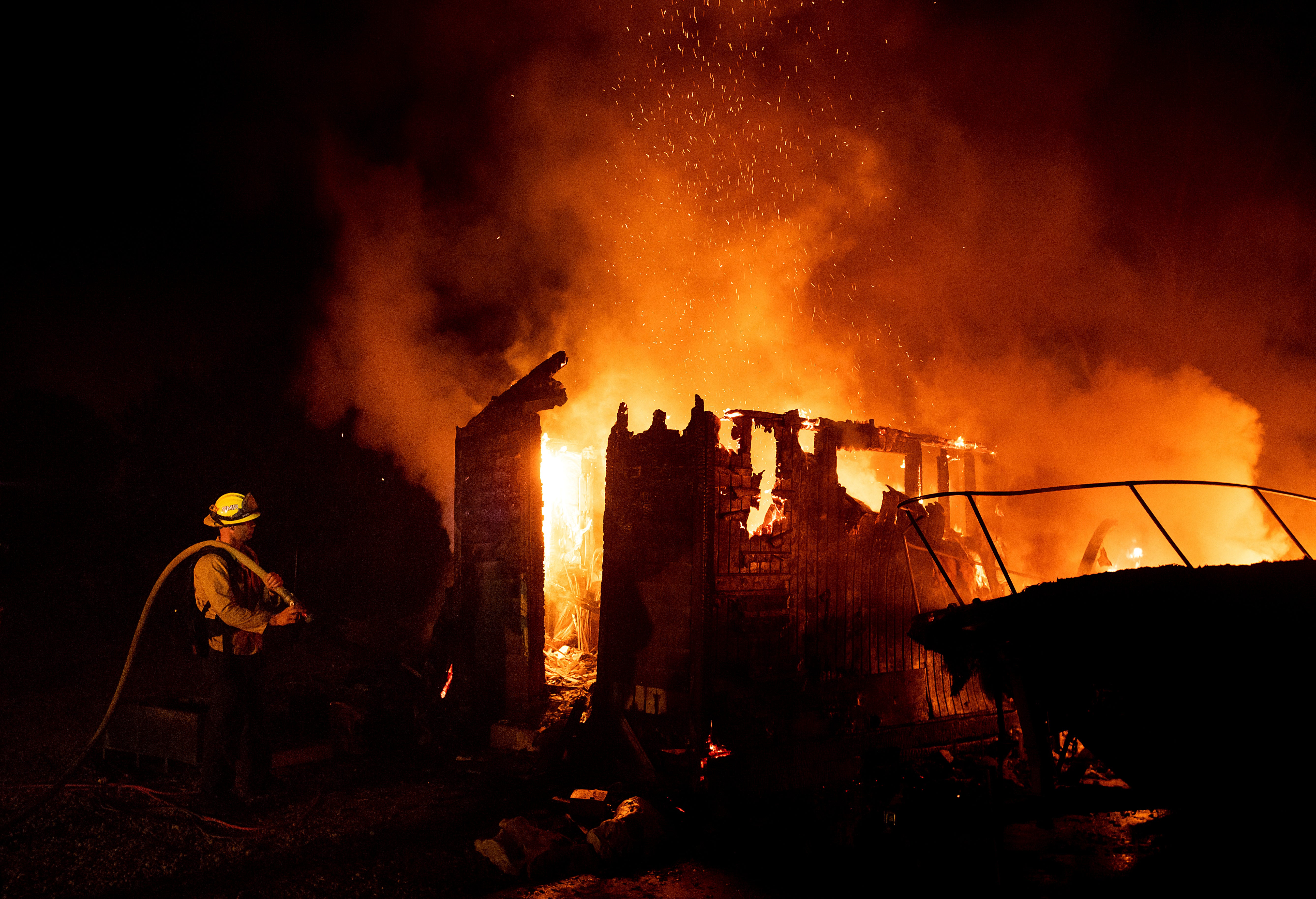 Firefighter Jay Wilkens monitors a flaming shed and boat as the Holiday fire burns in Goleta, Calif., on July 7, 2018. The blaze has destroyed multiple homes.