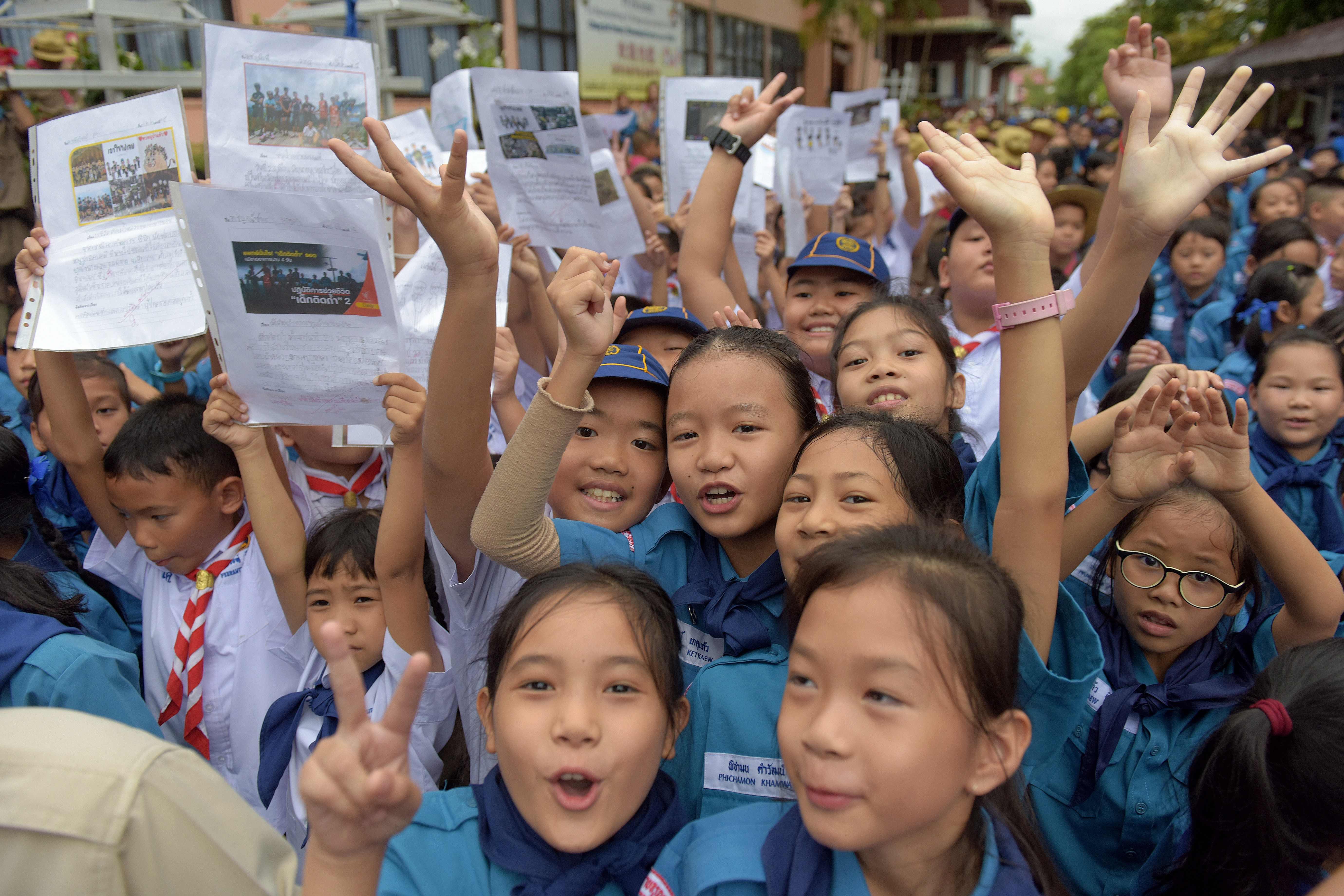 Thai students smile as they hold pictures of the 12 boys and football coach in front of the hospital where the group were brought for observation in Chiang Rai, Thailand on July 11, 2018.  The final five members of a young soccer team were rescued fro