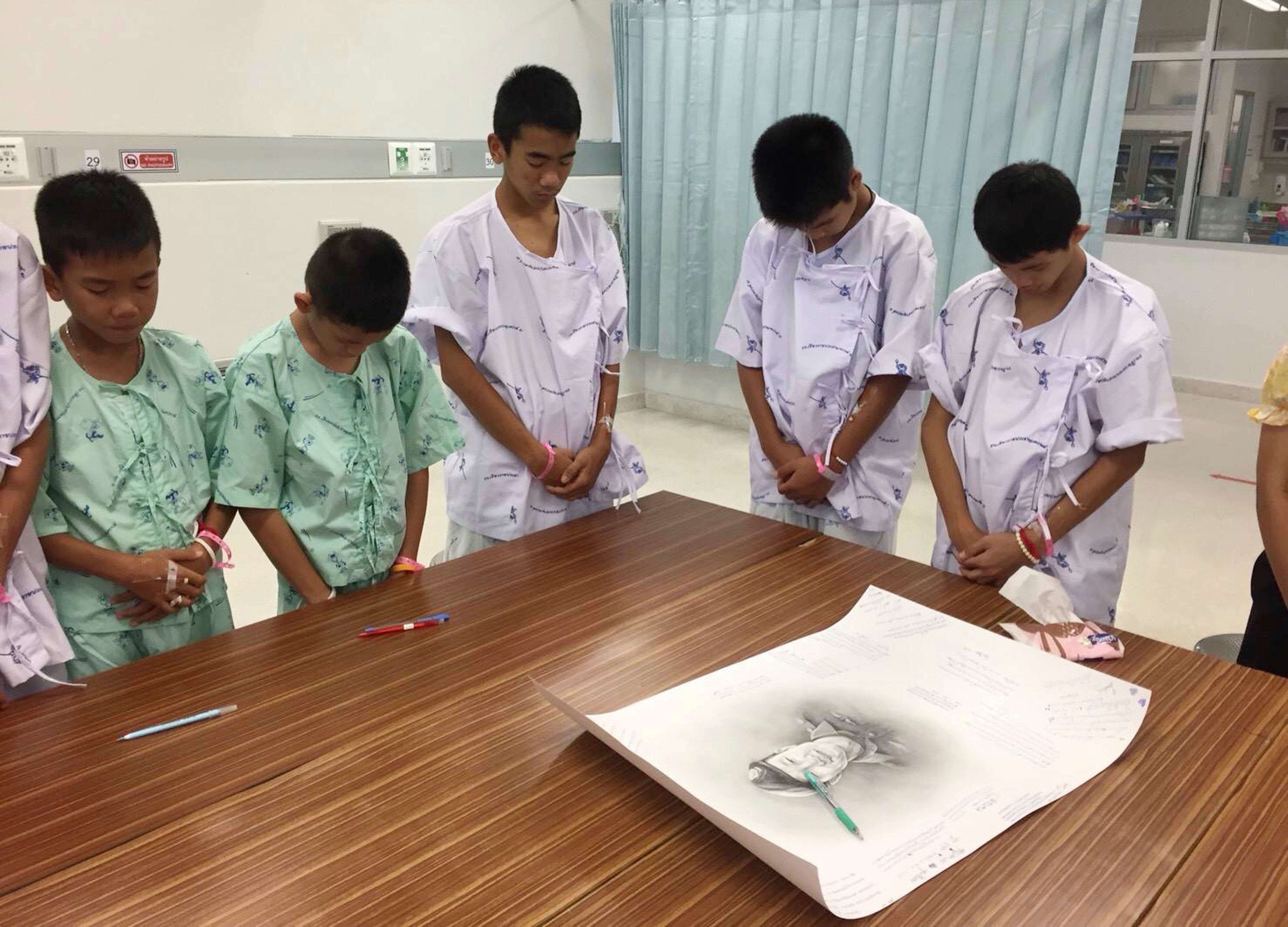 In this photo released by Thailand's Ministry of Health and the Chiang Rai Prachanukroh Hospital, some of the rescued soccer team members bow their heads respectfully in front of a sketch of the Thai Navy SEAL diver who died while trying to rescue th